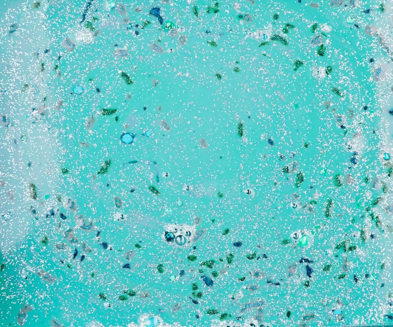 Жидкость аквамаринового цвета с разноцветными частицами.