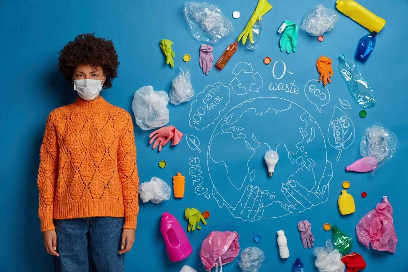 Этническая кудрявая женщина в защитной маске, одетая в вязаный оранжевый джемпер и джинсовые брюки, выглядит несчастной: её беспокоят загрязнение воздуха и серьёзная проблема загрязнения.